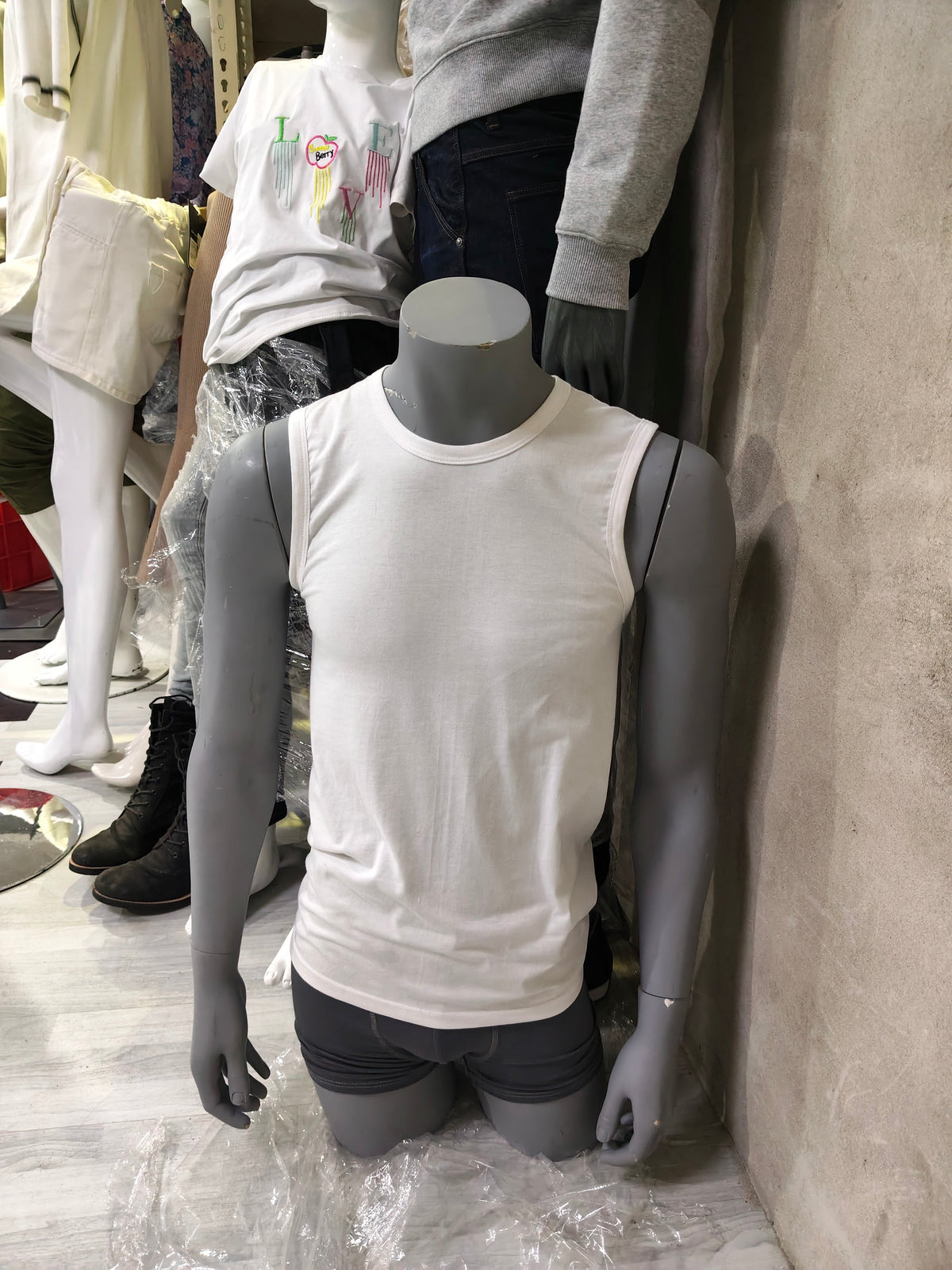 Grey male torso mannequin with white tank top, front view in storage
