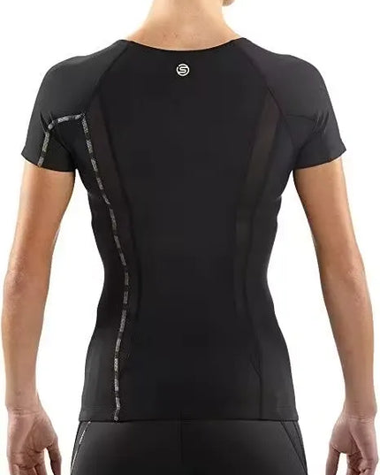 A woman athlete wearing a black SKINS Dnamic Women's Short Sleeve Top, performing a push-up exercise. Close-up of the SKINS Dnamic Women's Short Sleeve Top, highlighting the graduated compression zones and mesh panels. A group of diverse women athletes wearing SKINS Dnamic Women's Short Sleeve Tops in various colors, training together outdoors.