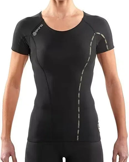 A woman athlete wearing a black SKINS Dnamic Women's Short Sleeve Top, performing a push-up exercise. Close-up of the SKINS Dnamic Women's Short Sleeve Top, highlighting the graduated compression zones and mesh panels. A group of diverse women athletes wearing SKINS Dnamic Women's Short Sleeve Tops in various colors, training together outdoors.