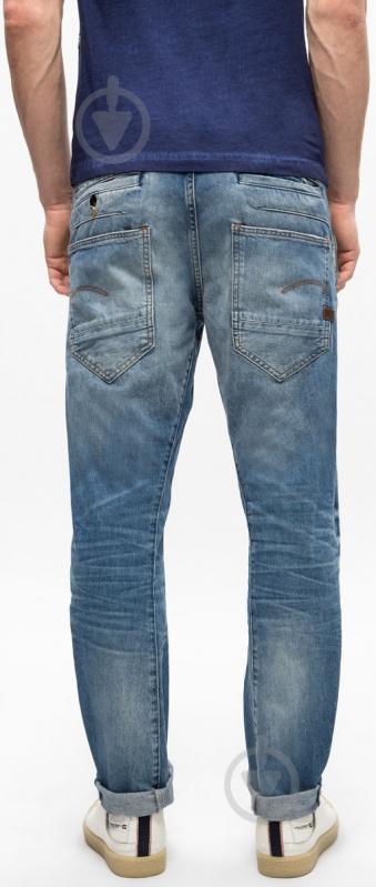 Back view of blue denim pants with a faded design and slim fit on a white background.