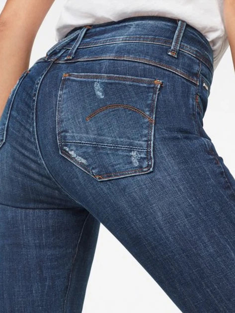 Close-up detail of blue skinny jeans highlighting back pocket design and stitching details on a white background