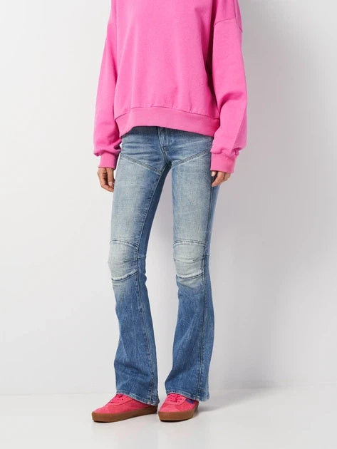 Lifestyle shot of flared jeans paired with a pink sweater against a white background.