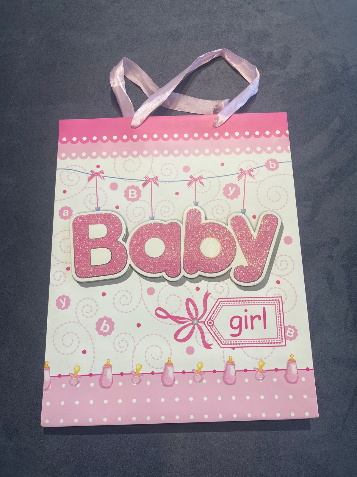 Baby girl pink gift bag with ribbon handles and Baby lettering, front view