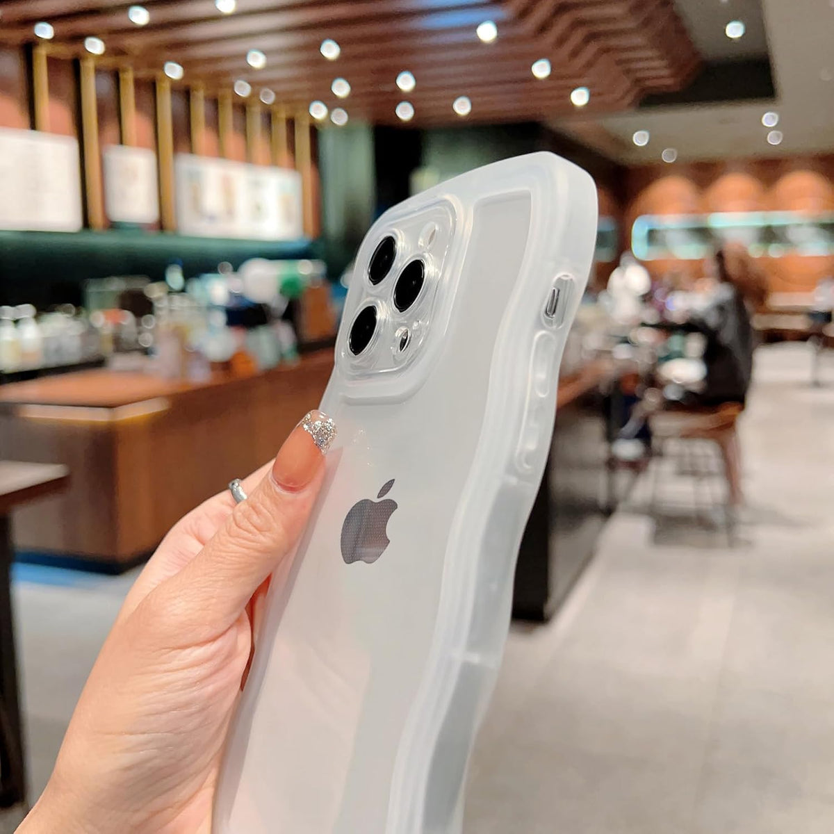 Hand holding iPhone 15 Pro Max in CEKKIENA clear wavy case in a cafe