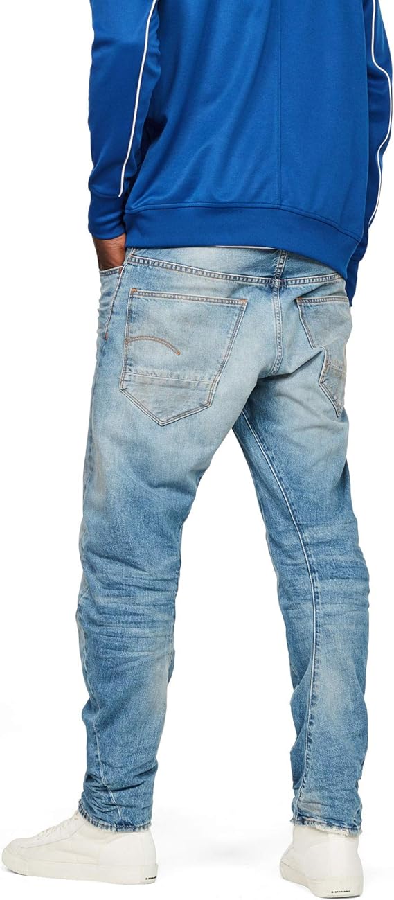 Back view of fitted blue jeans with sneakers, showcasing the denim's design against a white background.