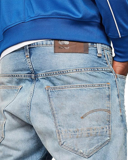 Detail close-up of light blue jeans showing back pockets and brand label on a white background.