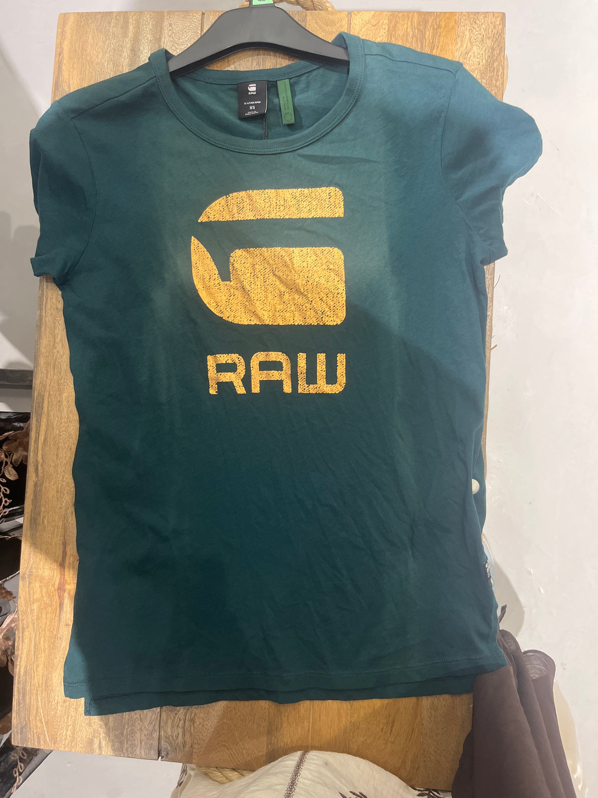 Green G-Star Raw T-shirt with gold RAW graphic hanging on a hanger