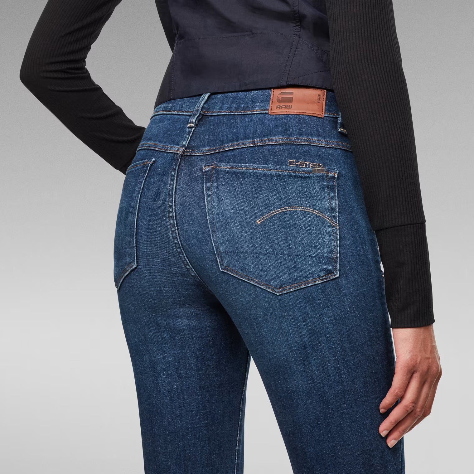 Detail close-up of medium blue skinny jeans featuring back pockets and brand patch.