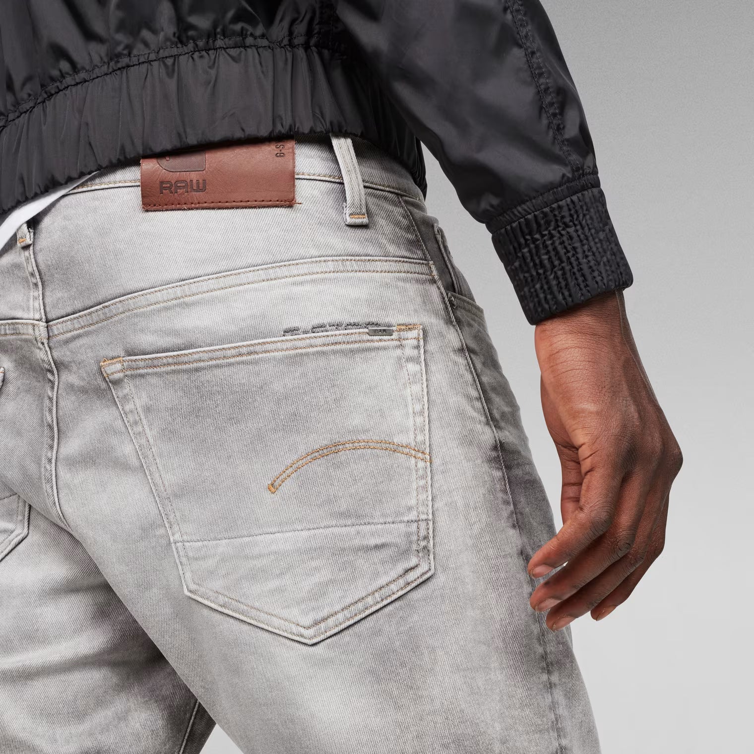 Detail close-up of the grey tapered jeans highlighting the back pocket and leather patch.