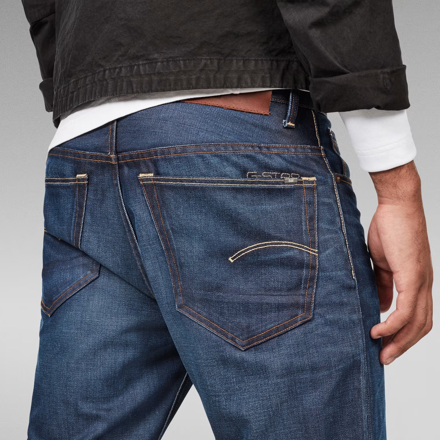 Detail close-up of dark blue jeans highlighting back pockets and stitching.