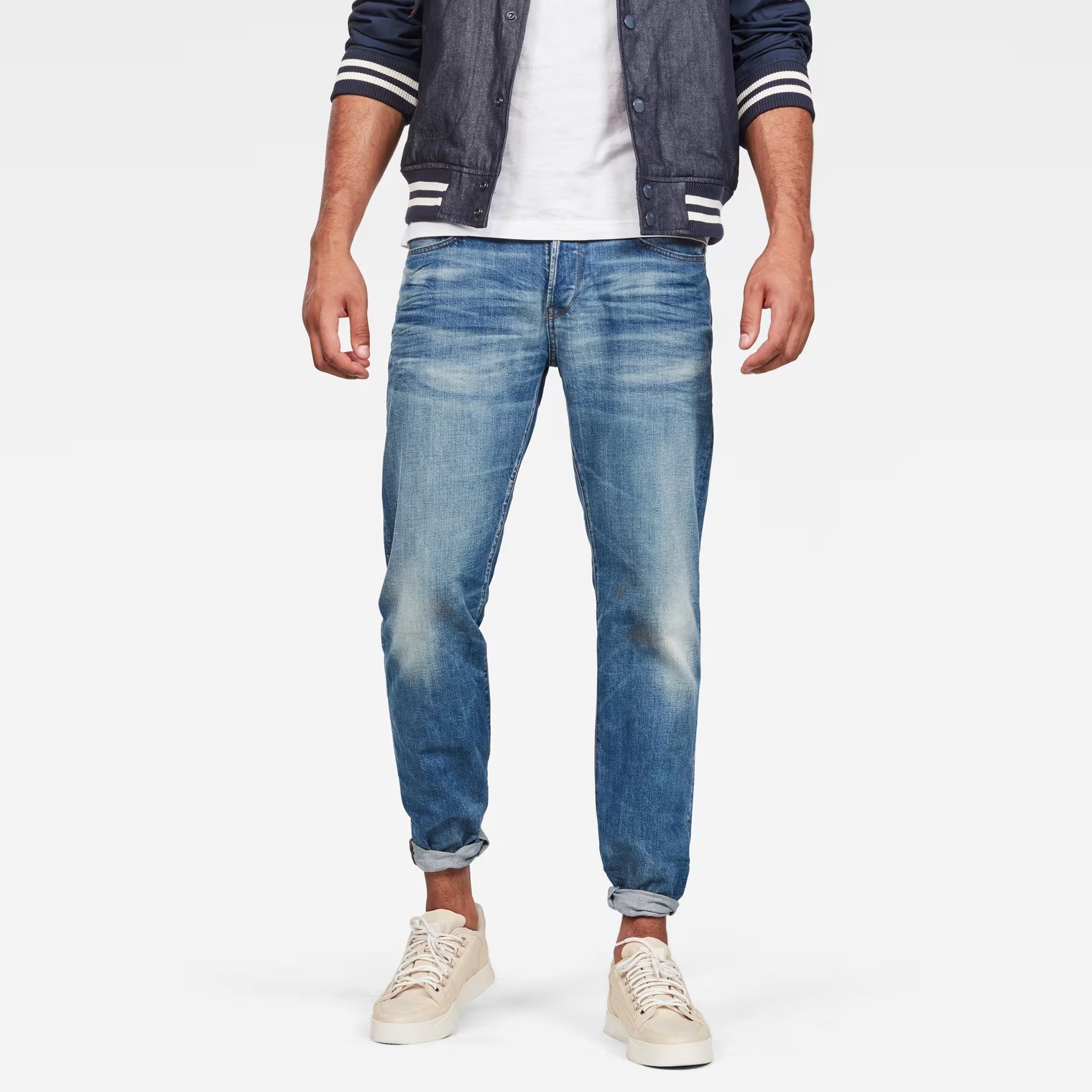 Lifestyle shot of relaxed straight jeans in medium blue with distressed details and five pockets.