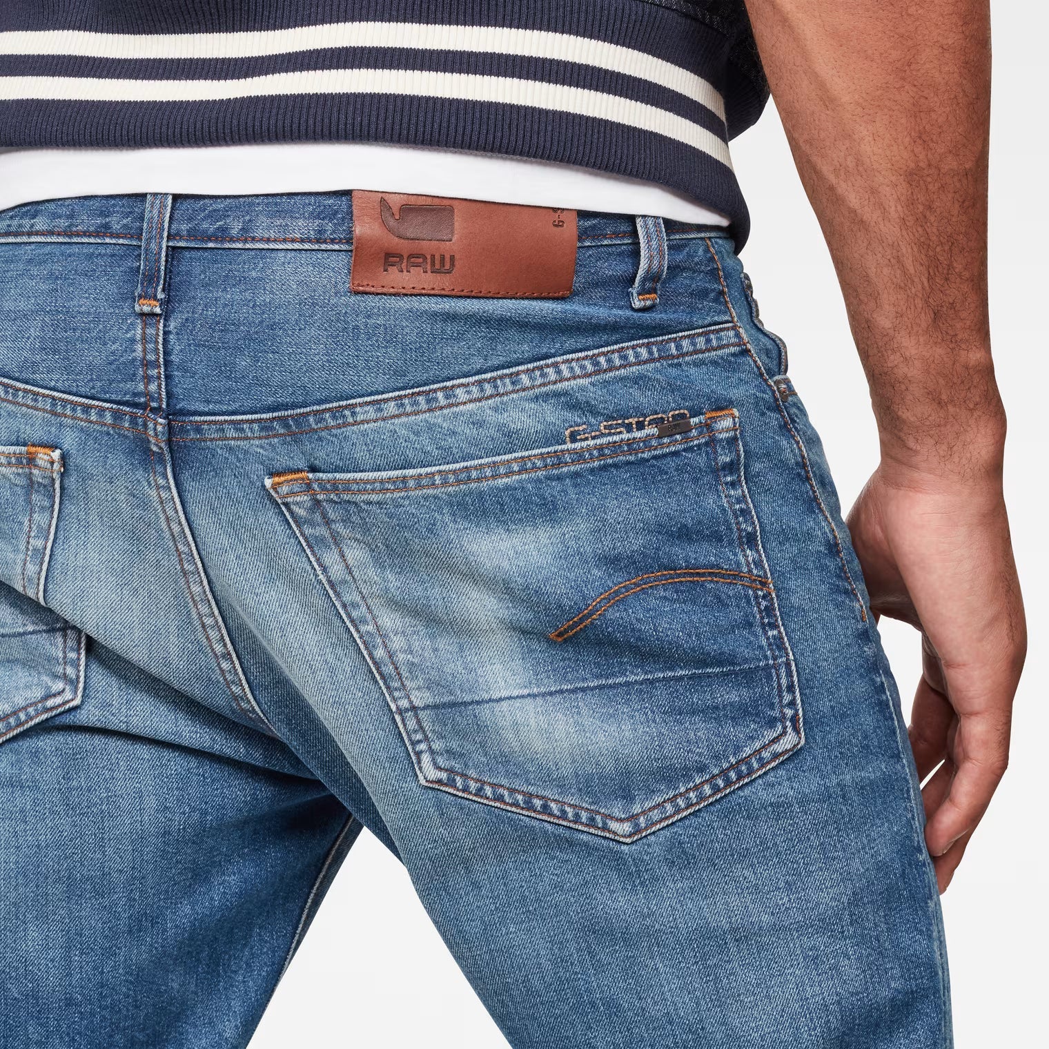 Detail close-up of the back of medium blue jeans showcasing leather patch and stitching details.