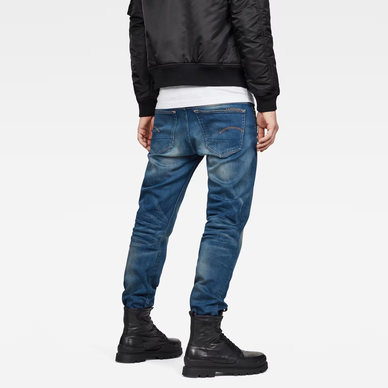 Lifestyle view of medium blue relaxed fit jeans featuring distressed details against a white backdrop.