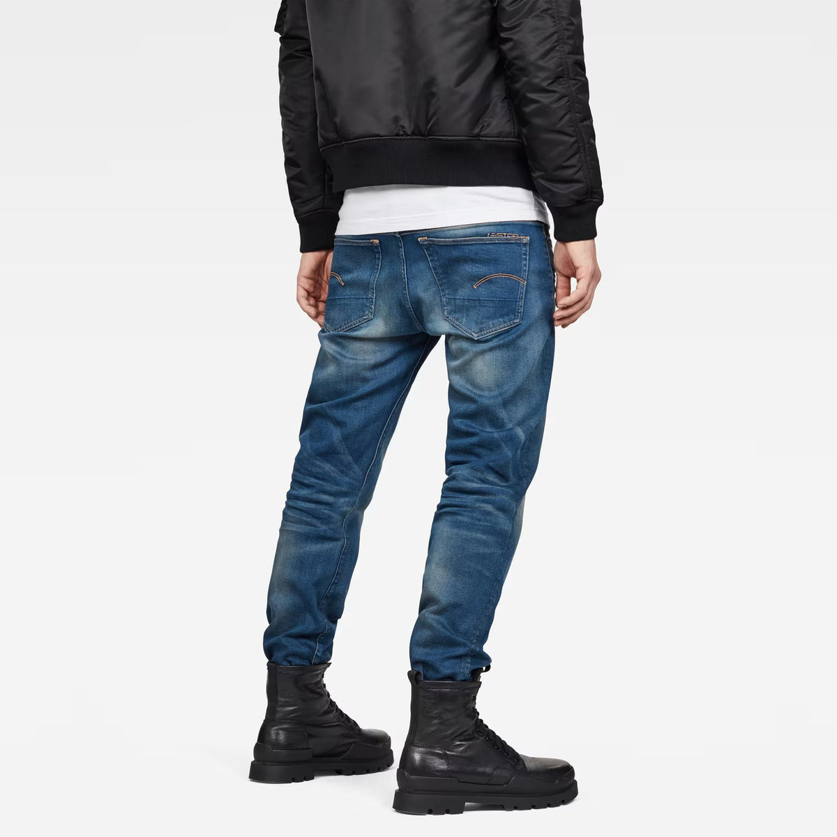 Lifestyle view of medium blue relaxed fit jeans featuring distressed details against a white backdrop.