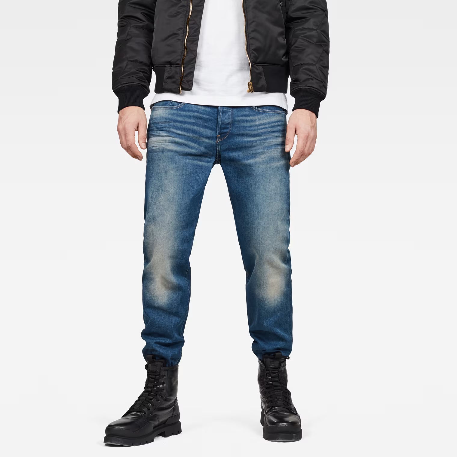 Lifestyle shot of medium blue relaxed fit jeans with distressed details on a white background.