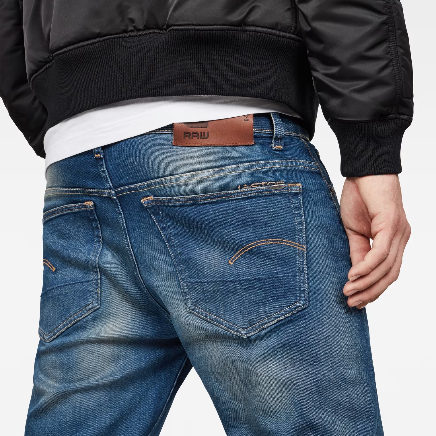 Close-up detail of medium blue jeans highlighting the back pocket design and brand label on a white background.
