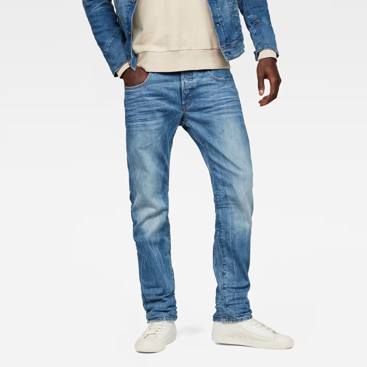Lifestyle shot of medium blue straight fit jeans with distressed details against a white background.