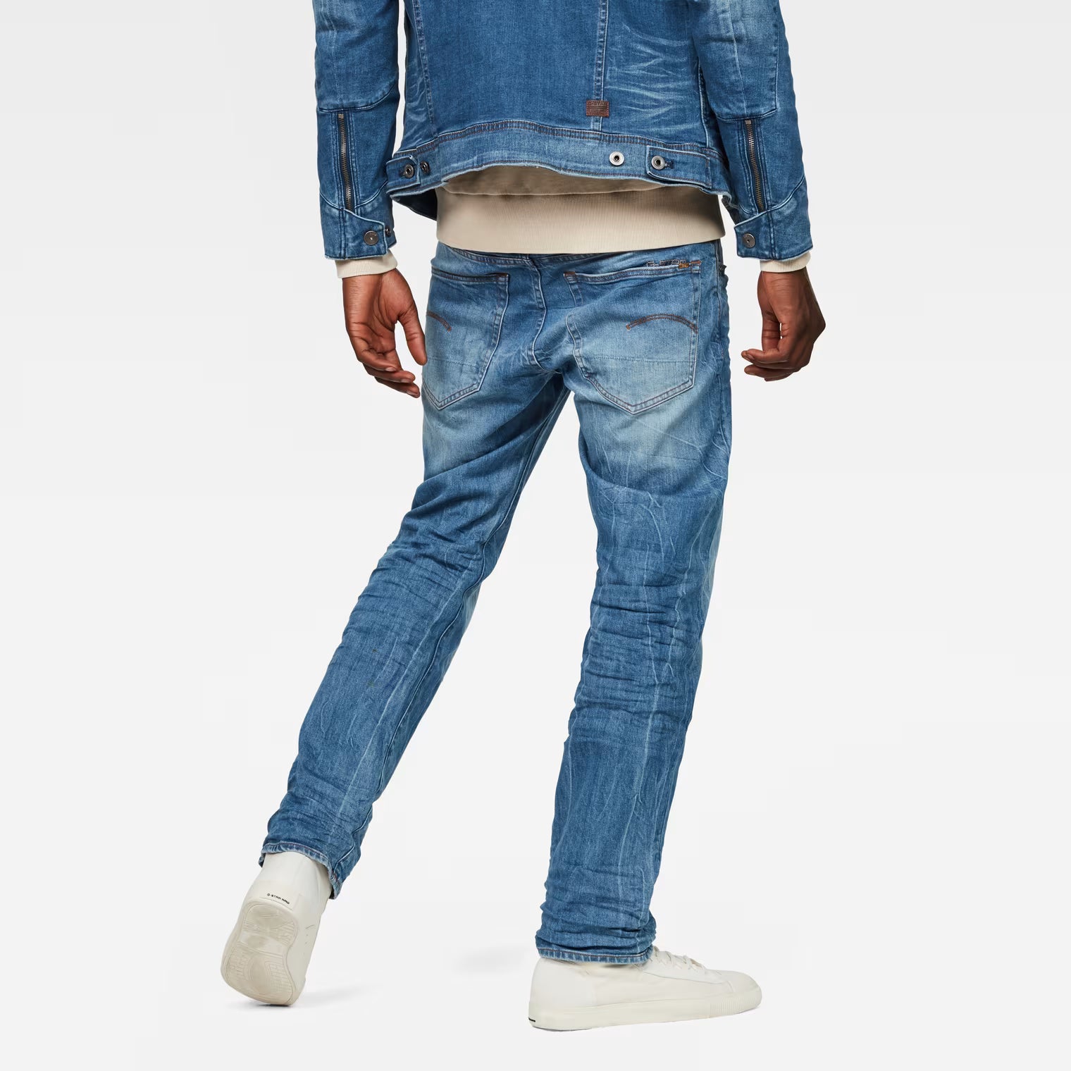 Back view of medium blue straight fit jeans showcasing distressed details on a white background.