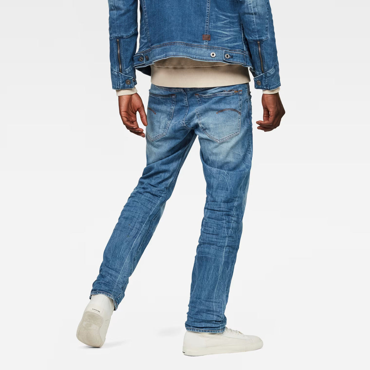Back view of medium blue straight fit jeans showcasing distressed details on a white background.