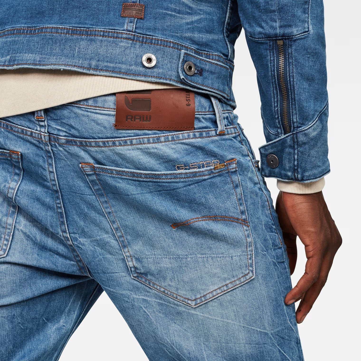 Detail close-up of medium blue jeans highlighting the back pocket and brand label on a white background.