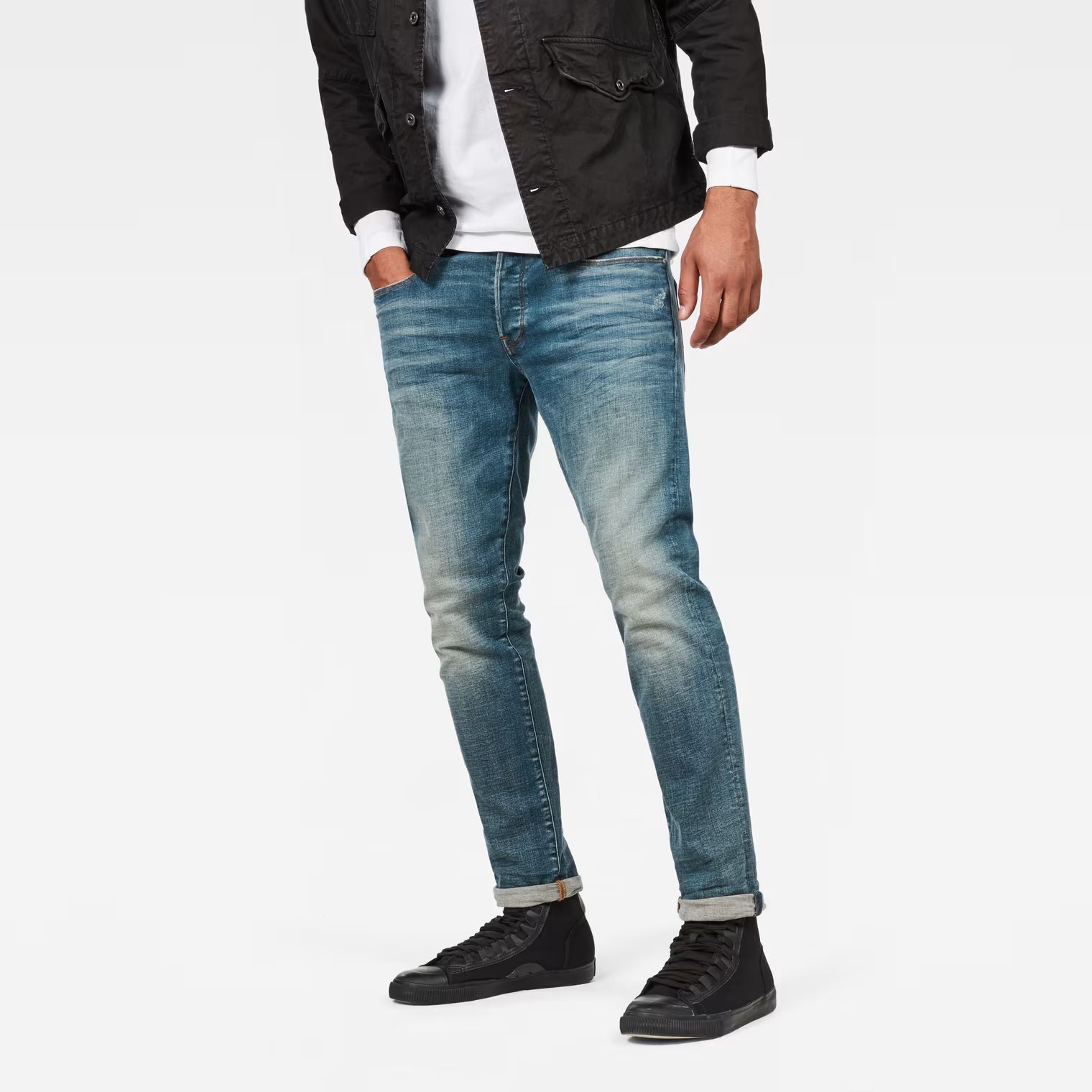 Lifestyle shot of medium blue straight tapered jeans with distressed details on a white background