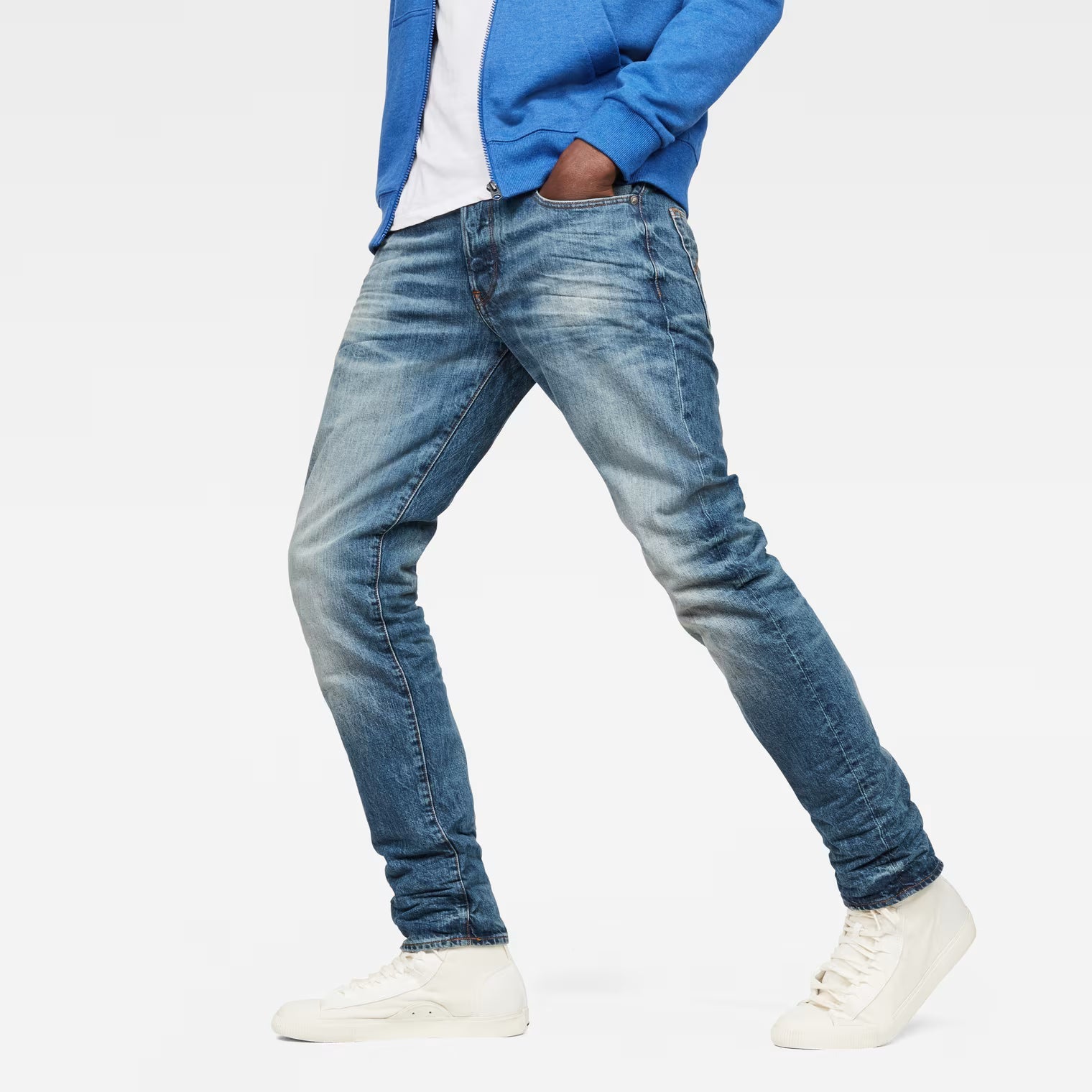 Lifestyle shot of medium blue jeans featuring a straight tapered fit and distressed details against a white background.