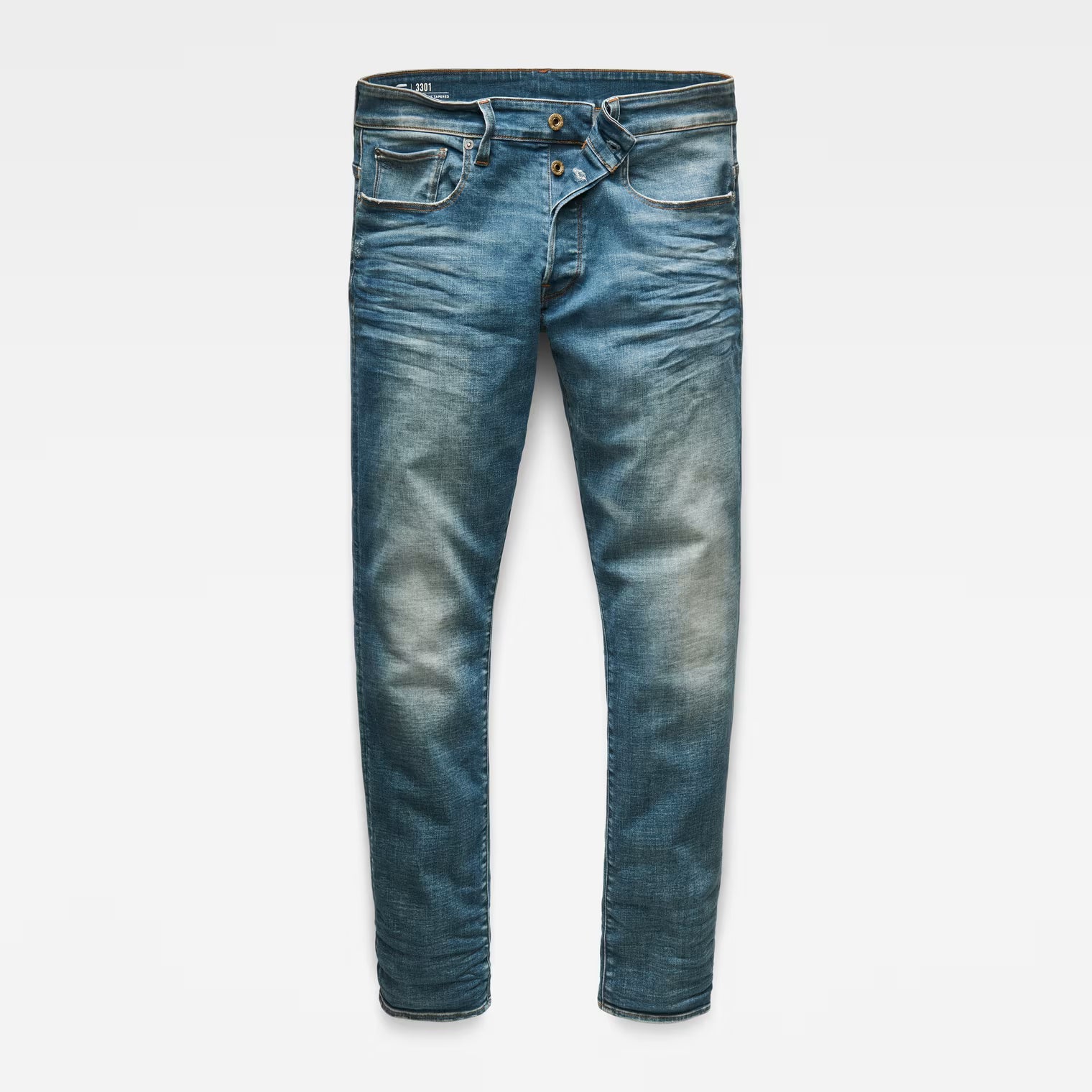 Front view of medium blue straight tapered jeans with distressed details on a white background