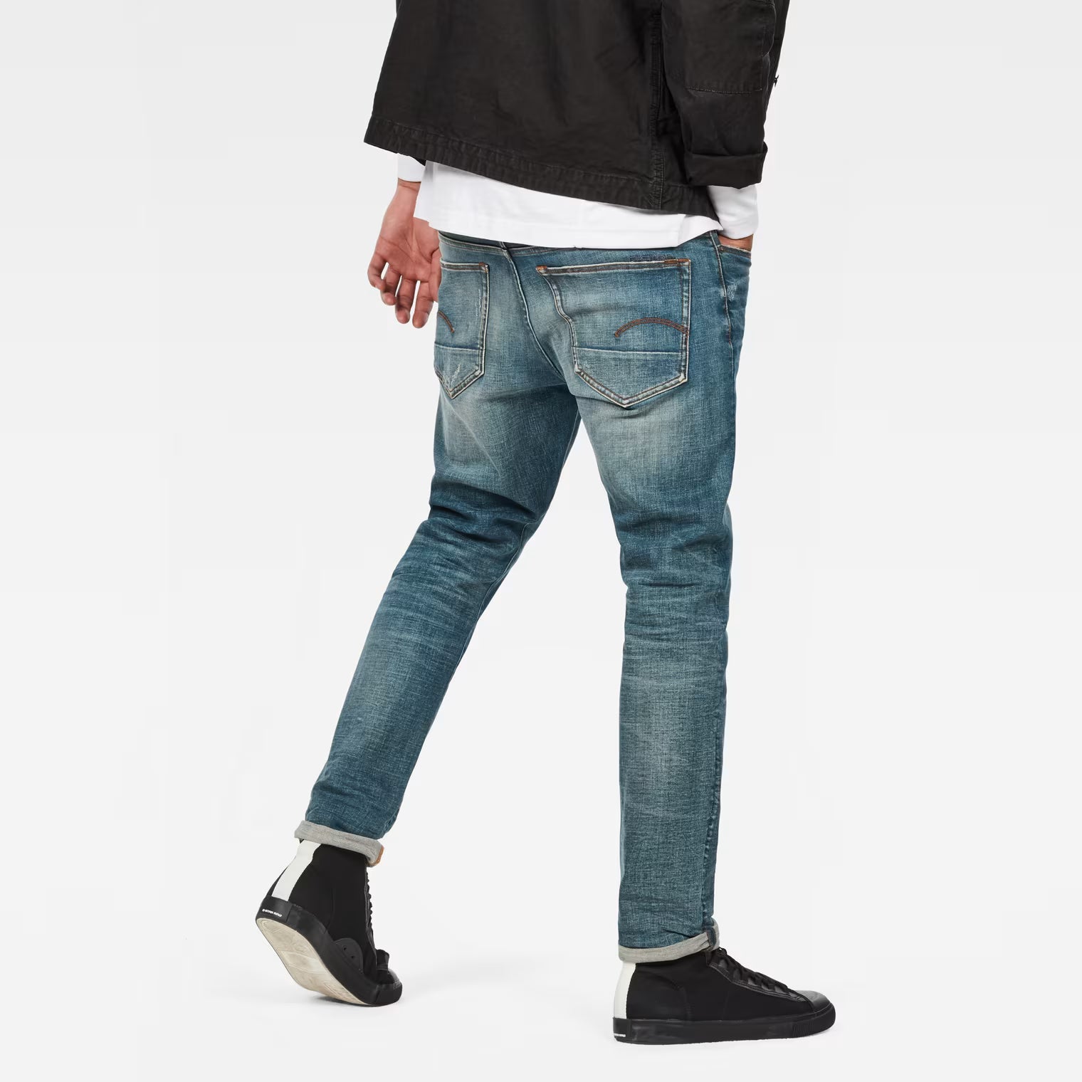 Back view of medium blue straight tapered jeans featuring distressed details on a white background
