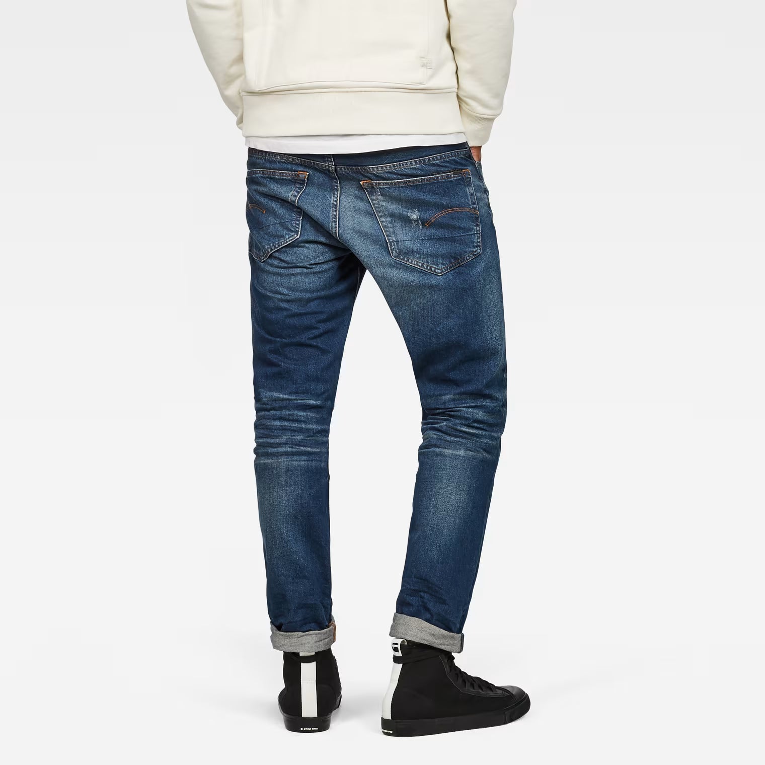 Back view of dark blue tapered jeans featuring distressed details on a white background.