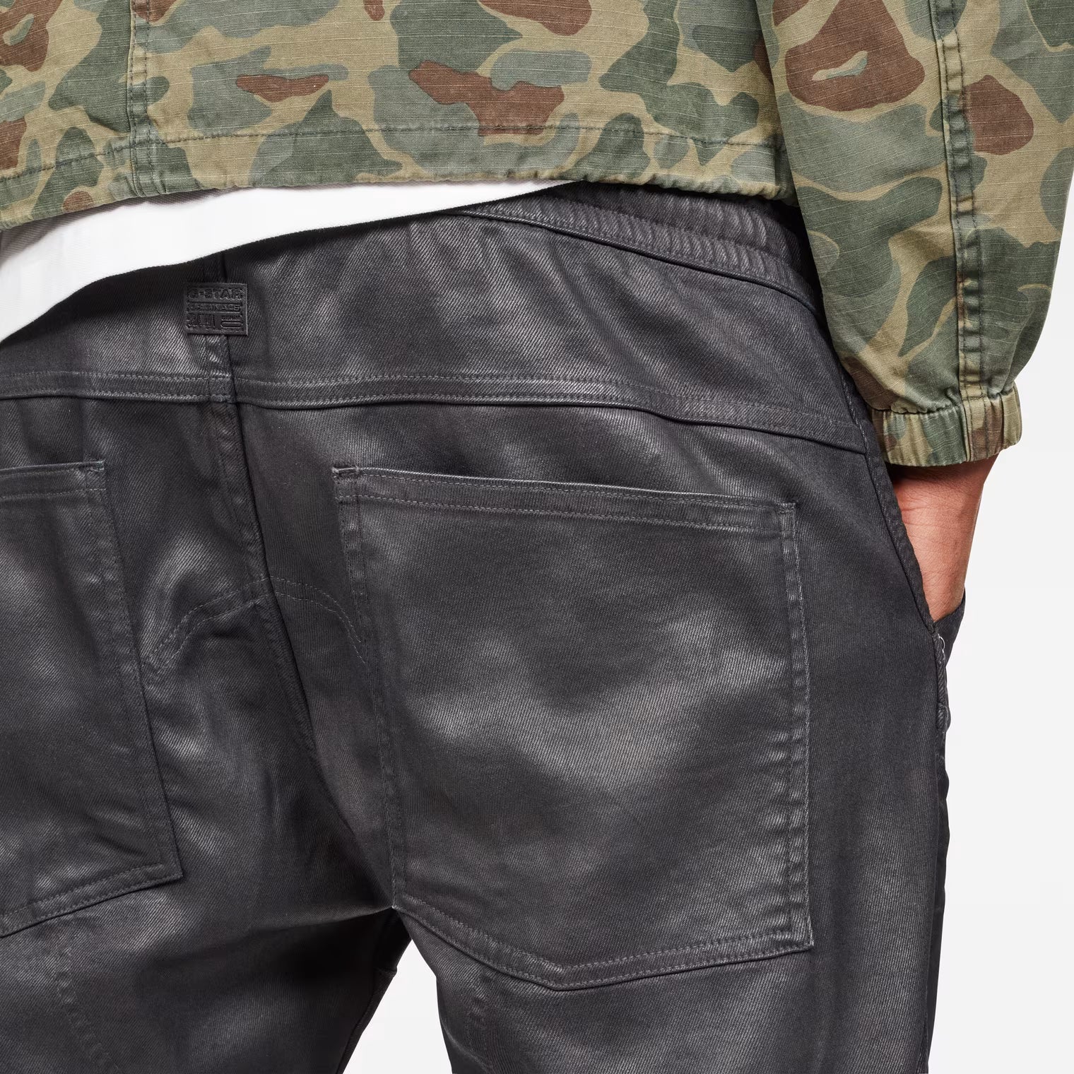 Detail close-up of the back pocket of grey tapered jeans with a 3D design on a white background.
