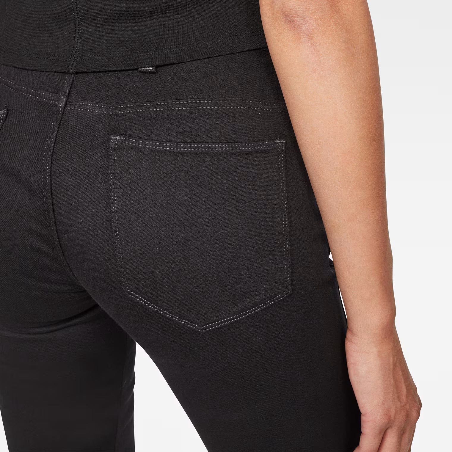 Detail close-up of black skinny jeans showing back pocket and skinny fit on a white background