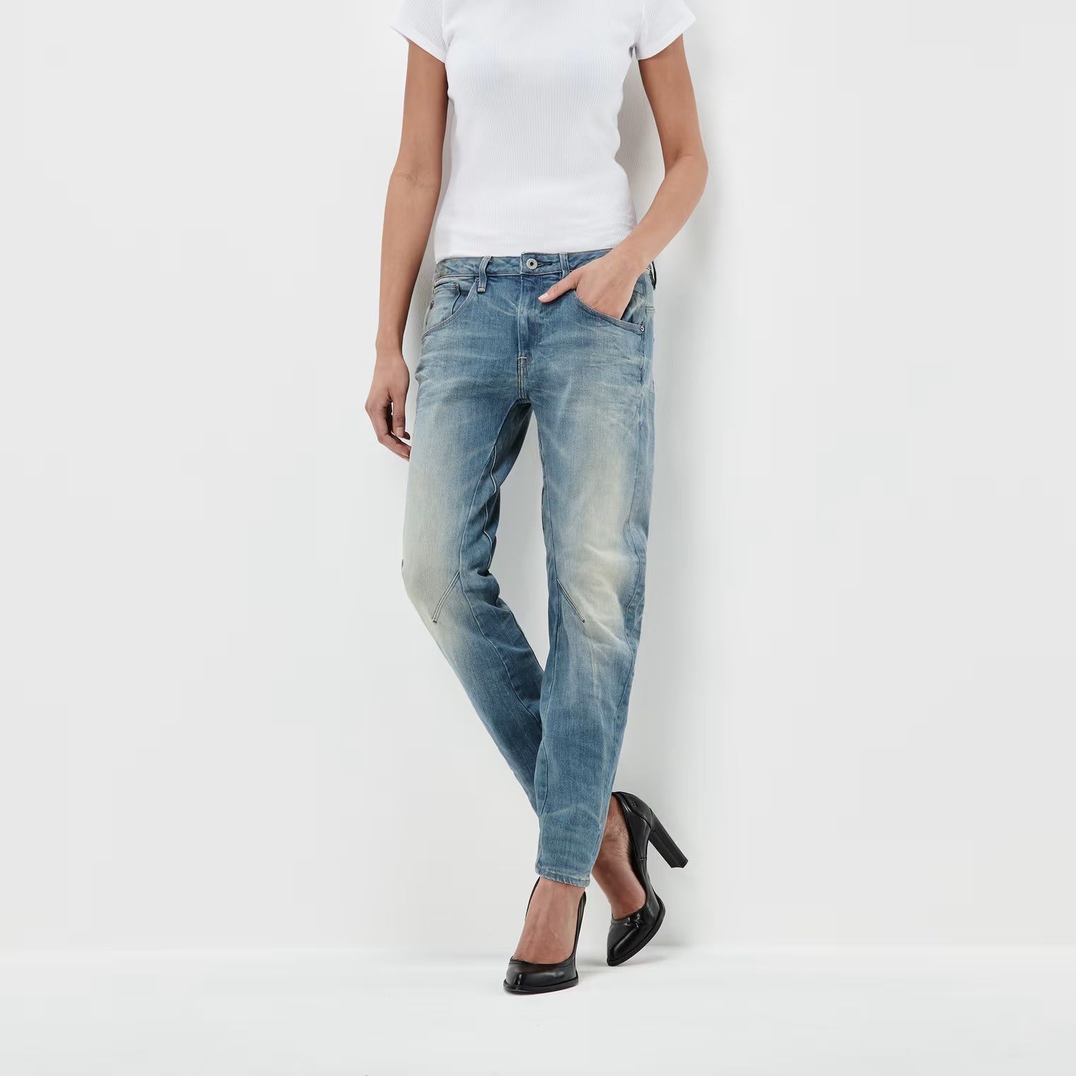 Lifestyle shot of medium blue boyfriend jeans with a low waist and distressed look on a white background.