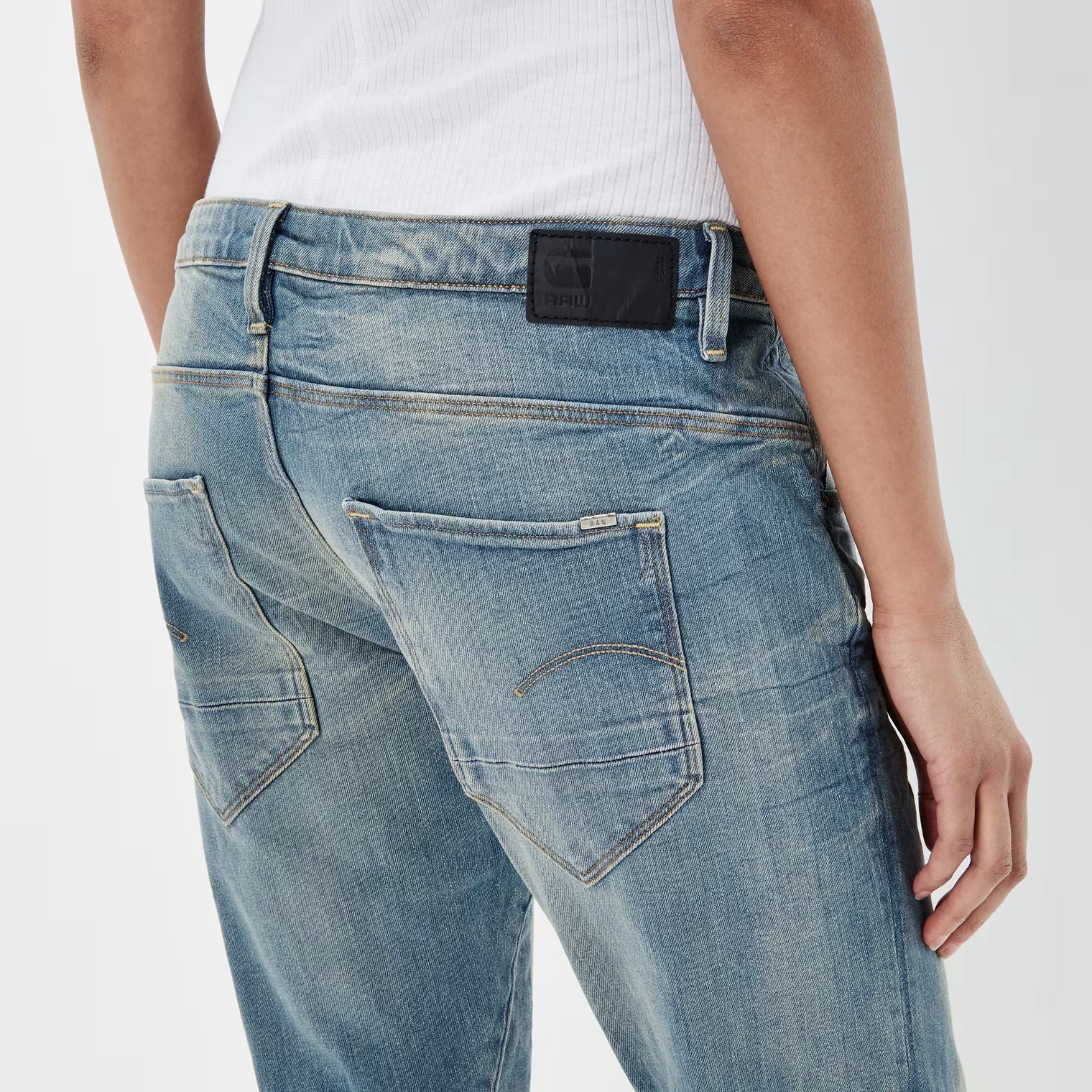 Detail close-up of medium blue boyfriend jeans showing back pockets and label tag on a white background.