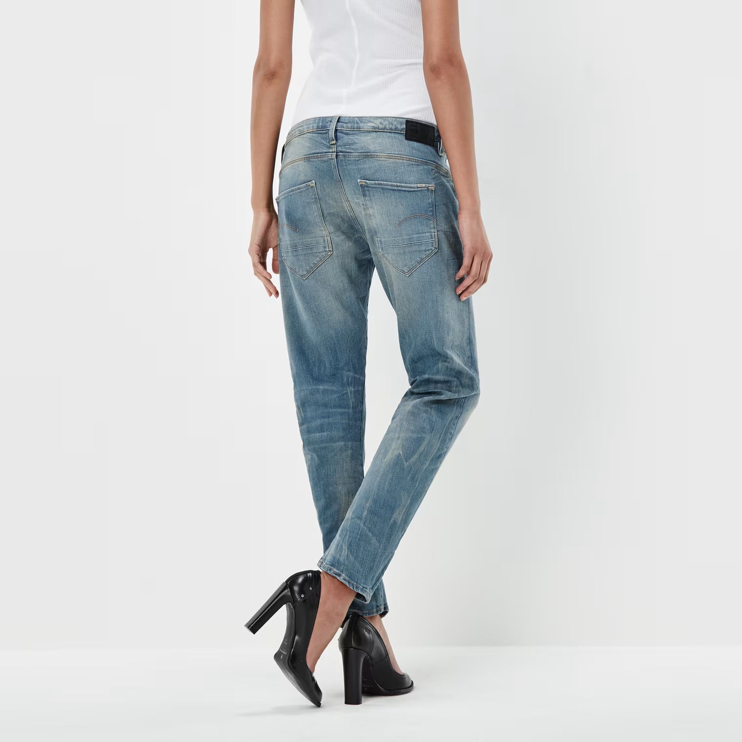 Back view of medium blue boyfriend jeans featuring a low waist and distressed look against a white background.
