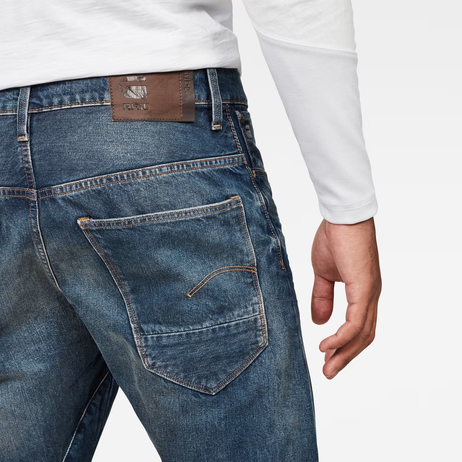Detail close-up of dark blue jeans highlighting back pockets and brown label on a white background.