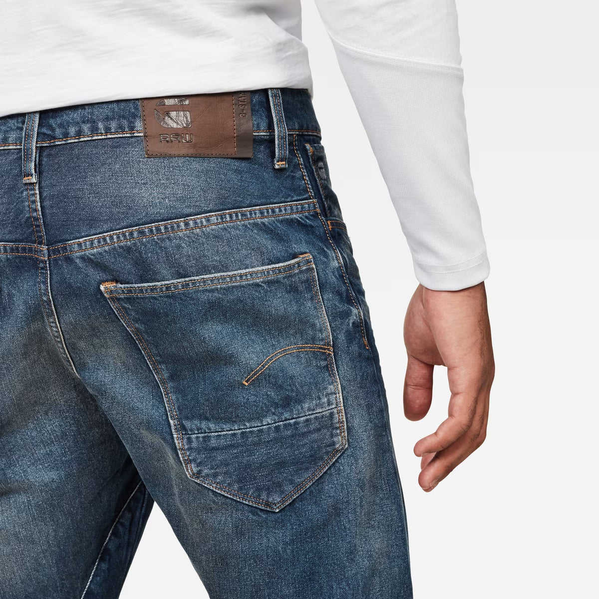 Detail close-up of dark blue jeans highlighting back pockets and brown label on a white background.