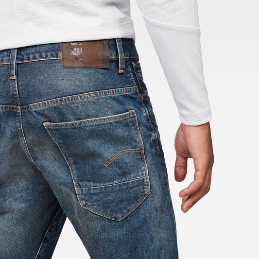 Detail close-up of dark blue jeans highlighting back pockets and brown label on a white background.