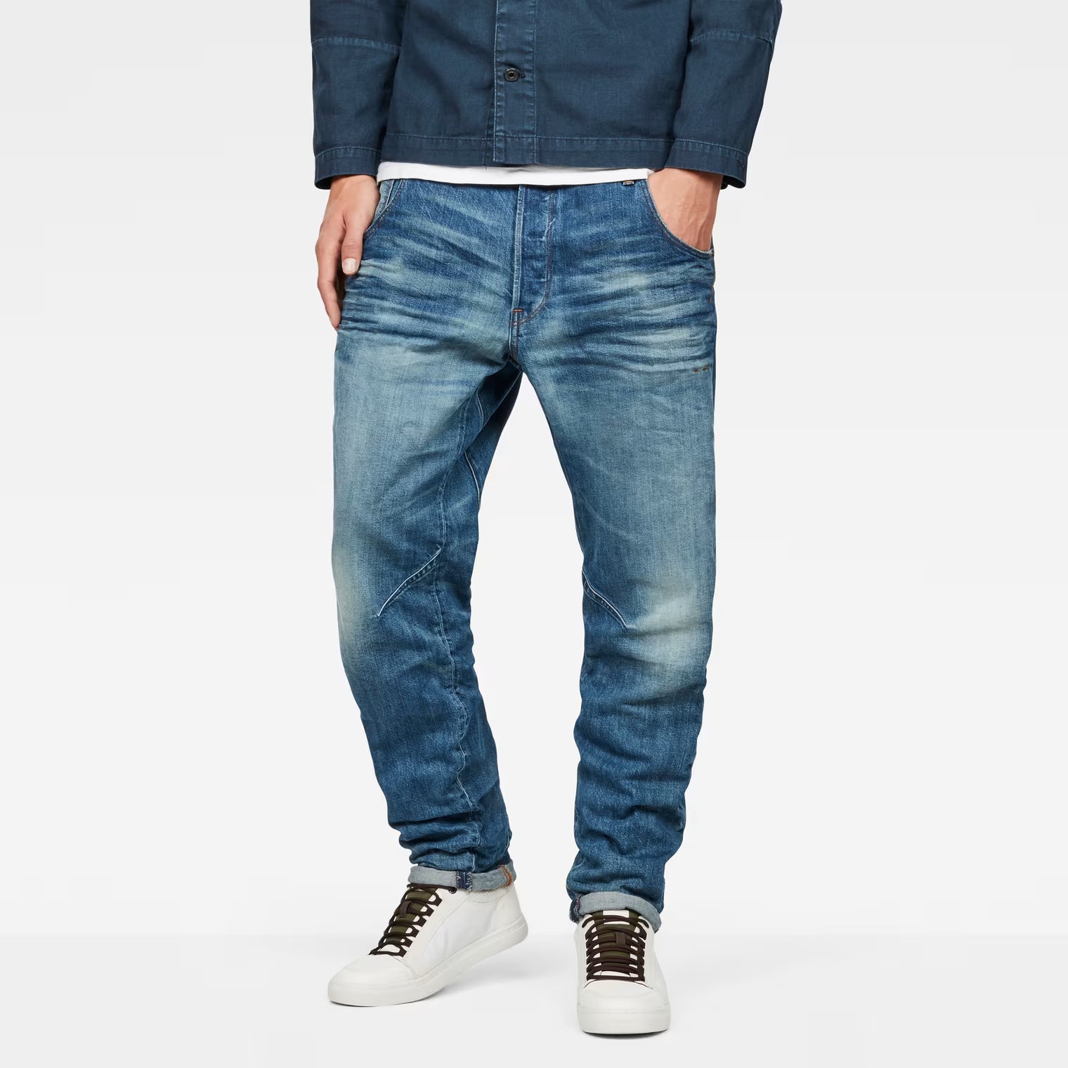 Lifestyle shot of medium blue tapered jeans featuring distressed details and a slim fit.