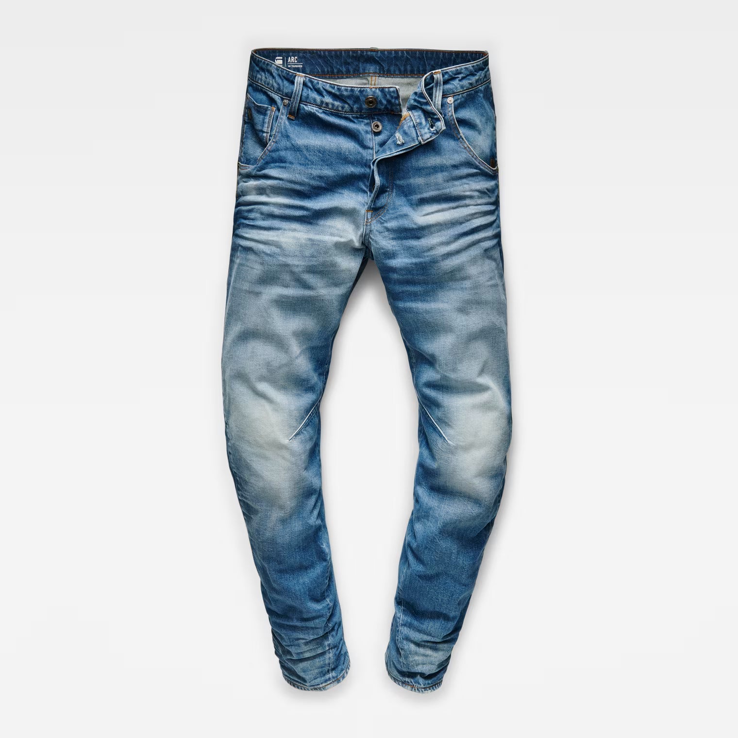 Front view of medium blue tapered jeans with a skinny fit and distressed details.