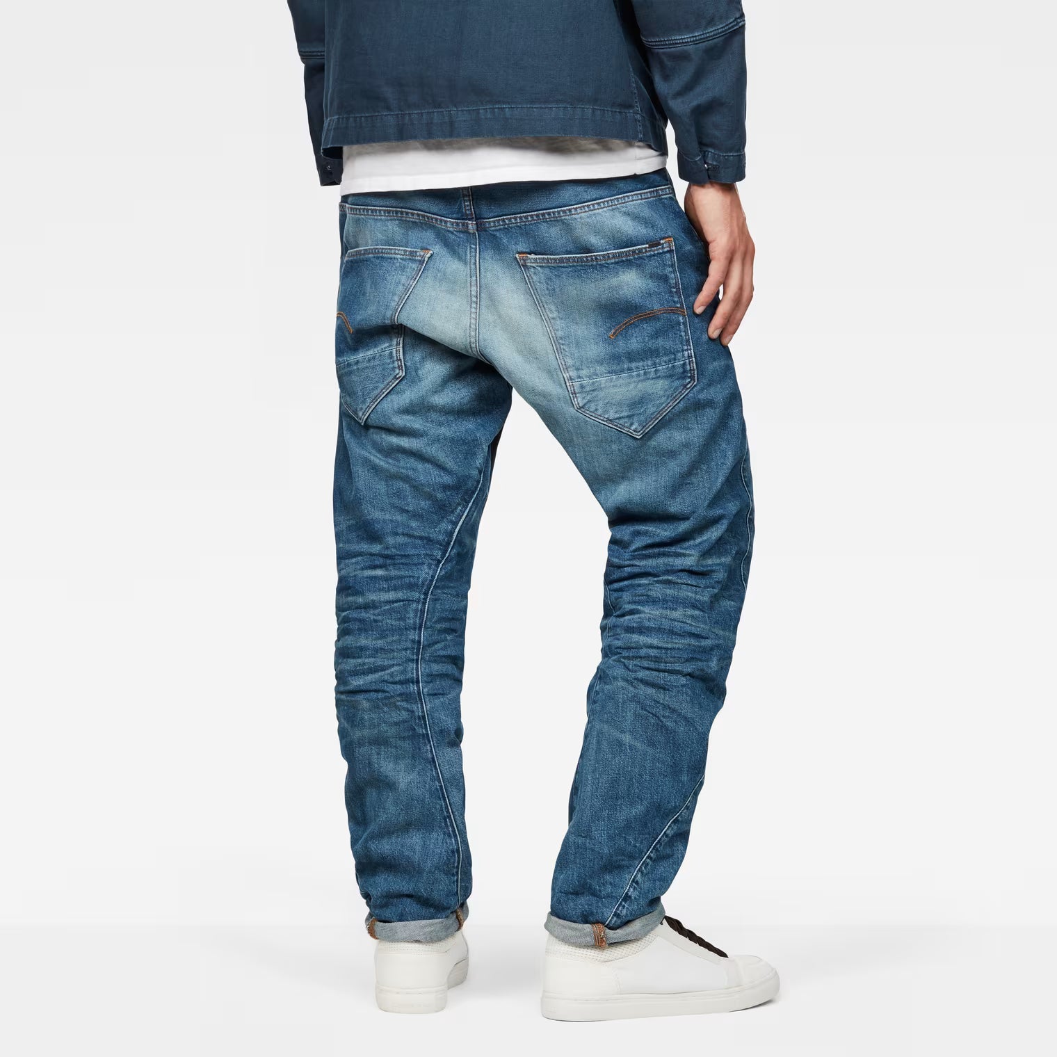 Back view of medium blue tapered jeans showcasing distressed details and back pockets.