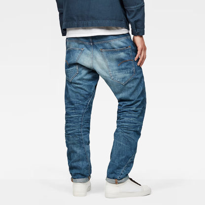 Back view of medium blue tapered jeans showcasing distressed details and back pockets.