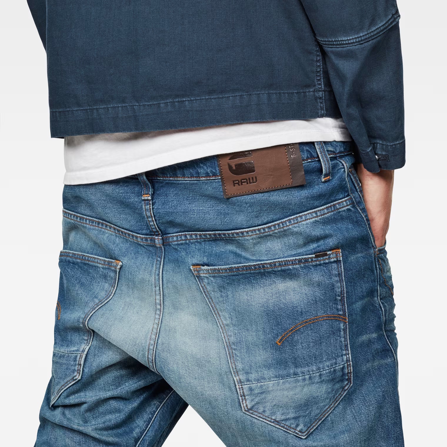 Detail shot of medium blue tapered jeans highlighting the back view and brand patch.