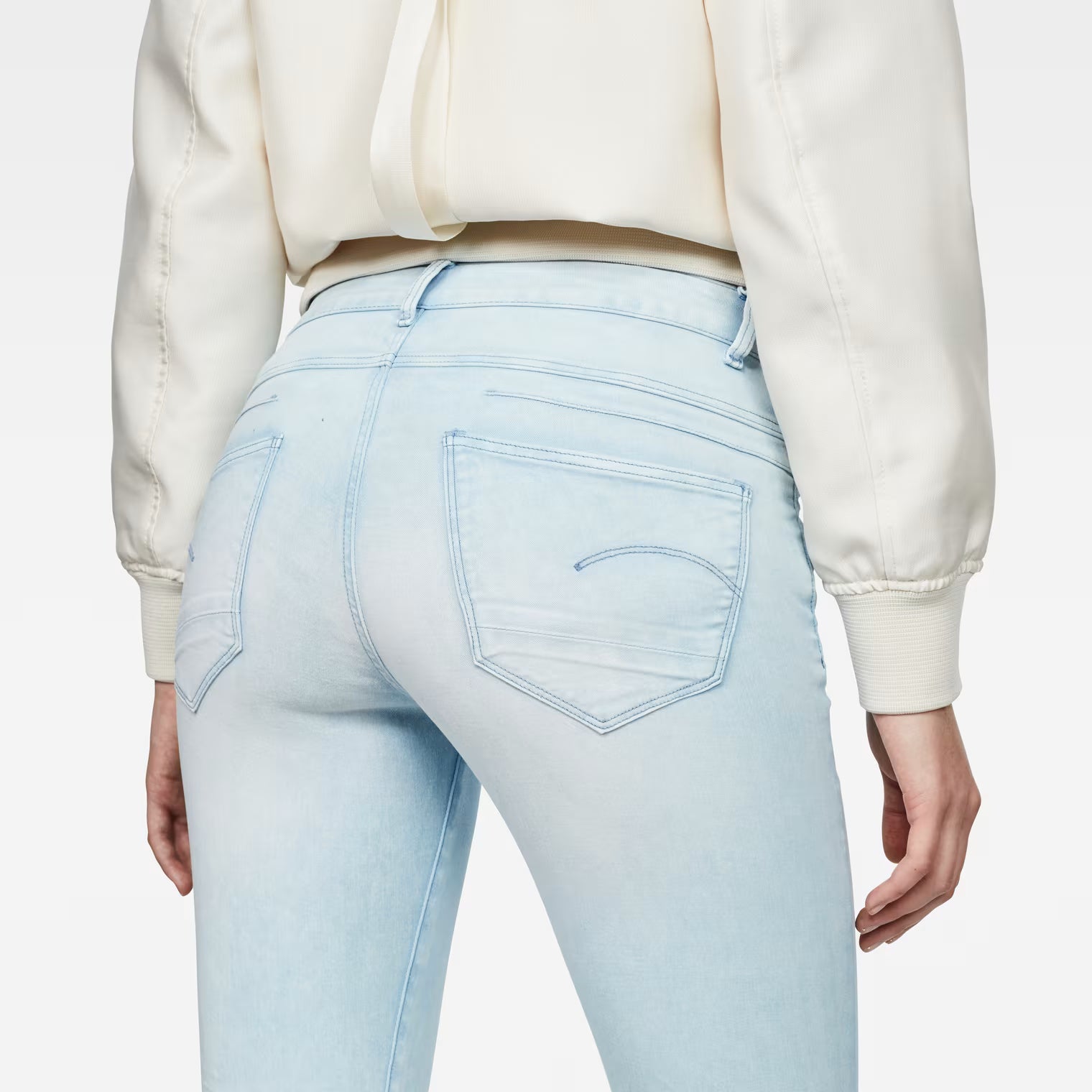 Detail close-up of light blue skinny jeans highlighting the 5-pocket design on a white background.