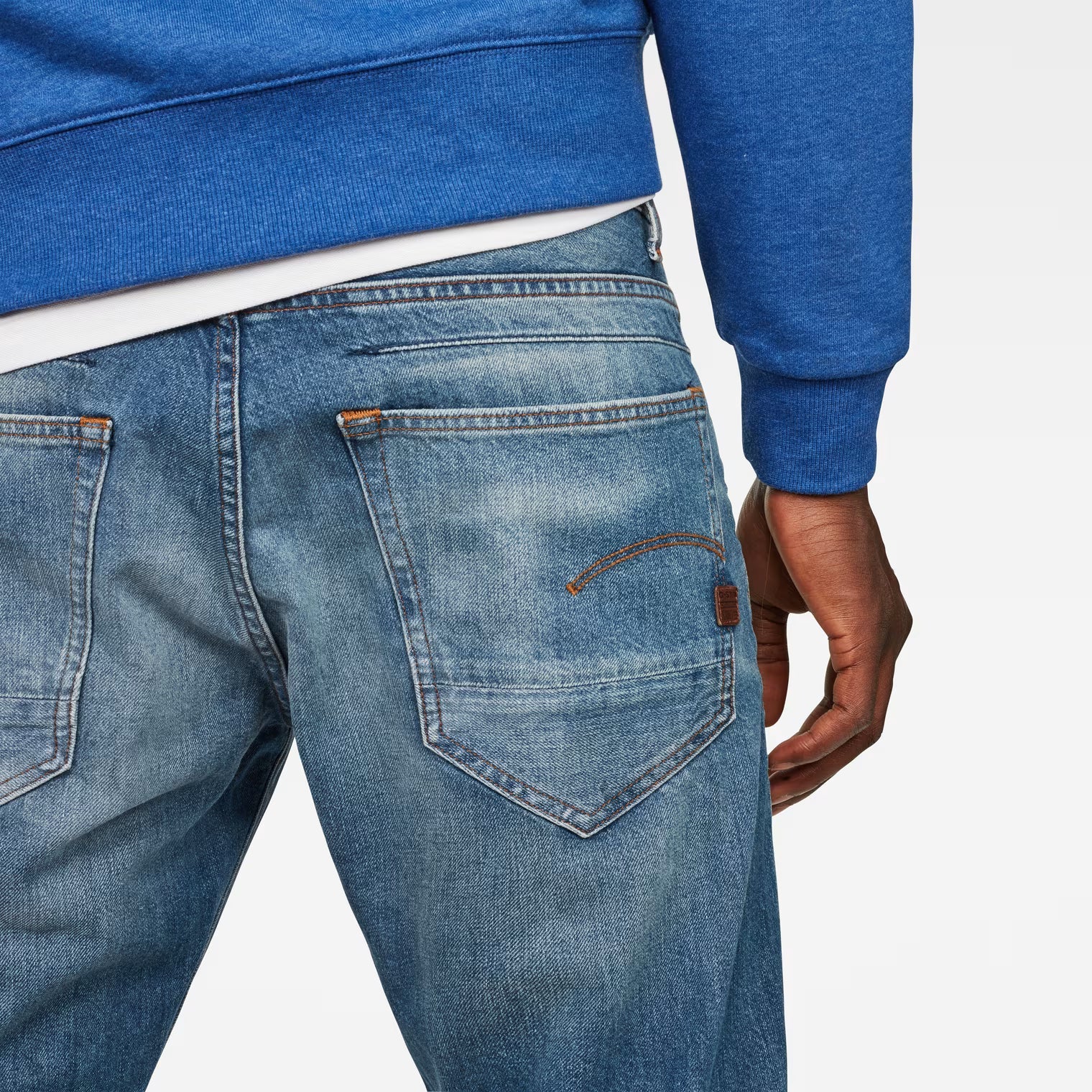 Detail close-up of tapered blue jeans highlighting the 5-pocket design on a white background.