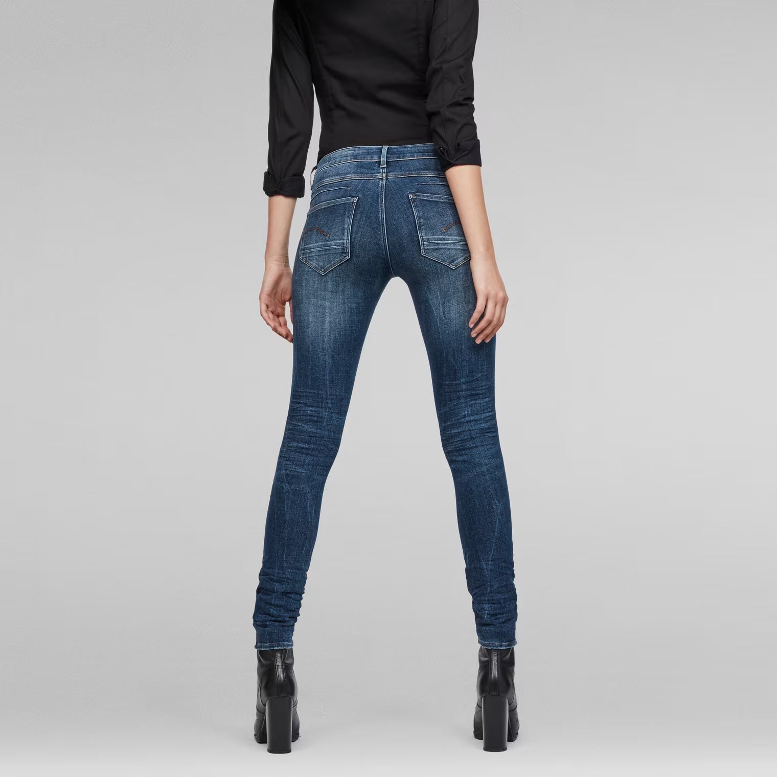 Back view of medium blue skinny jeans highlighting the mid waist fit.