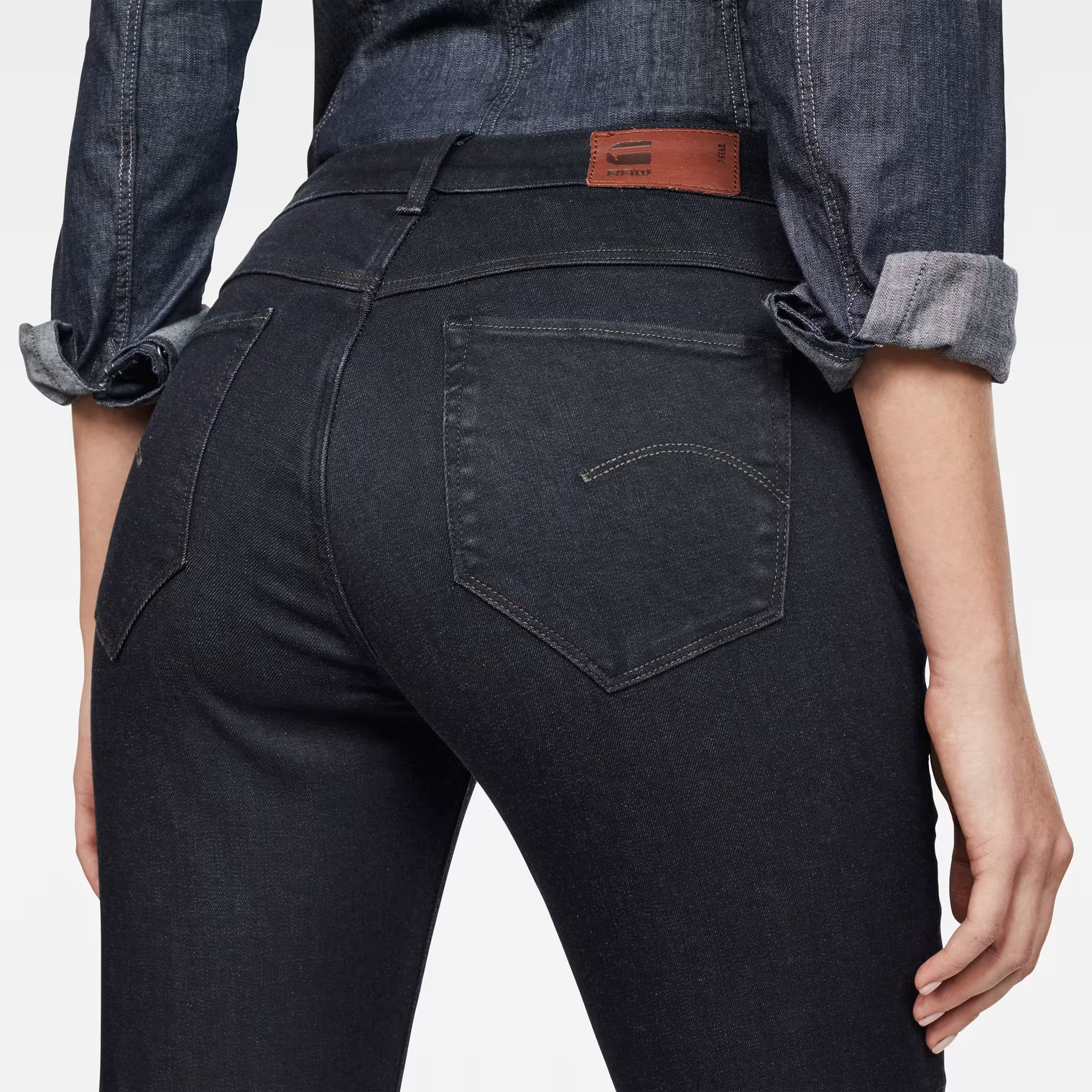 Detail shot of black skinny jeans highlighting back pockets and high waist on a white background.