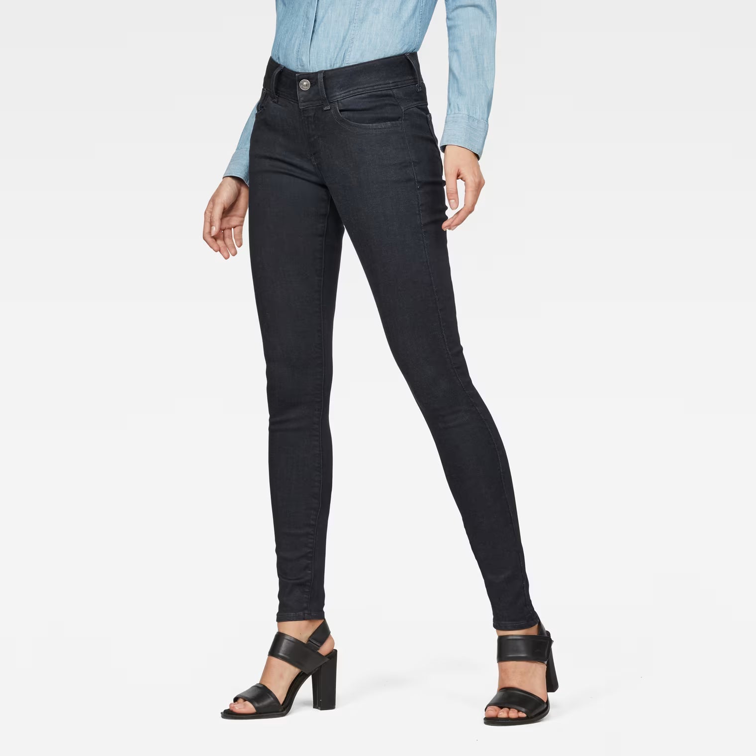 Lifestyle shot of black super skinny jeans with a mid-rise fit against a white background.