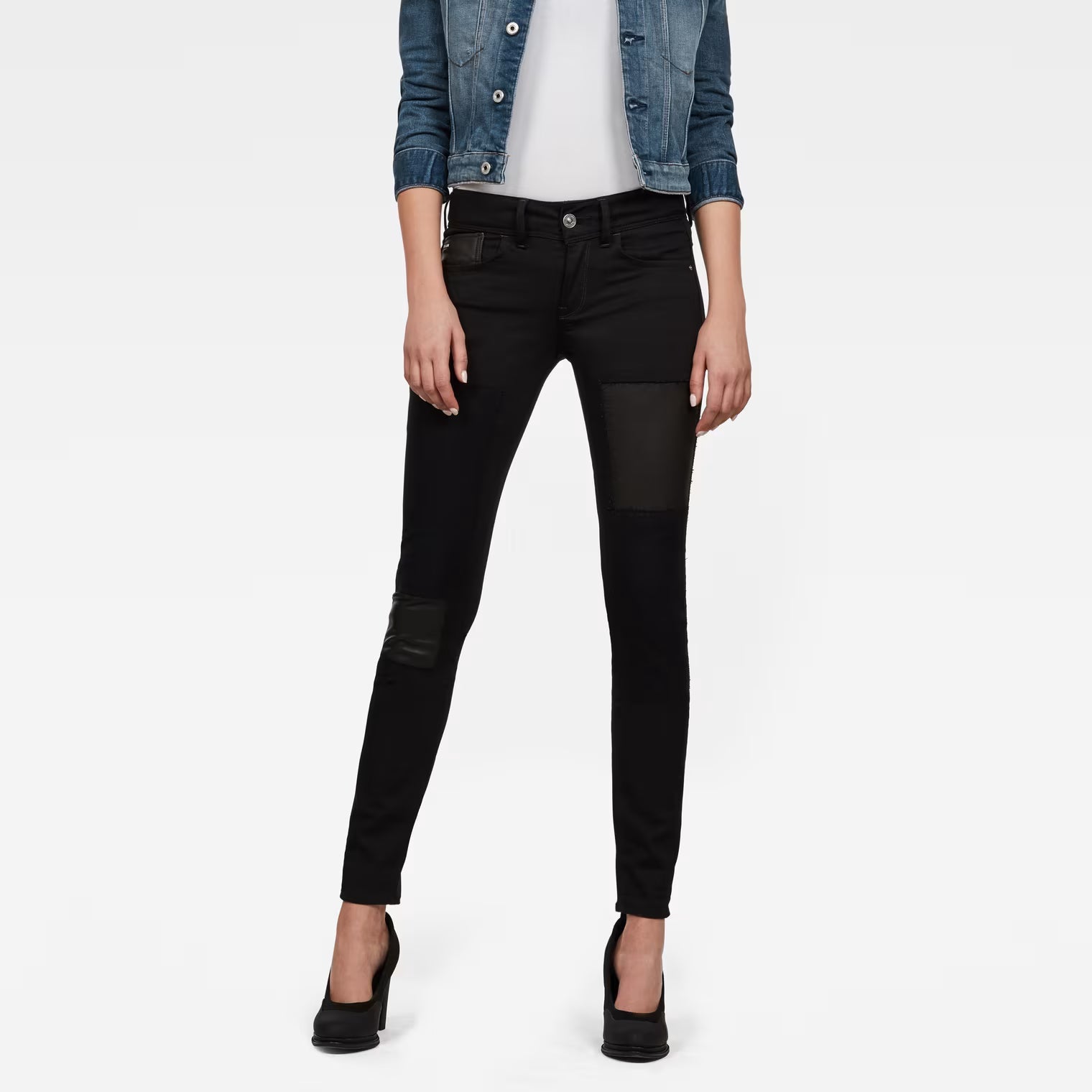 Lifestyle shot of black skinny jeans with mid-rise fit against a white background.
