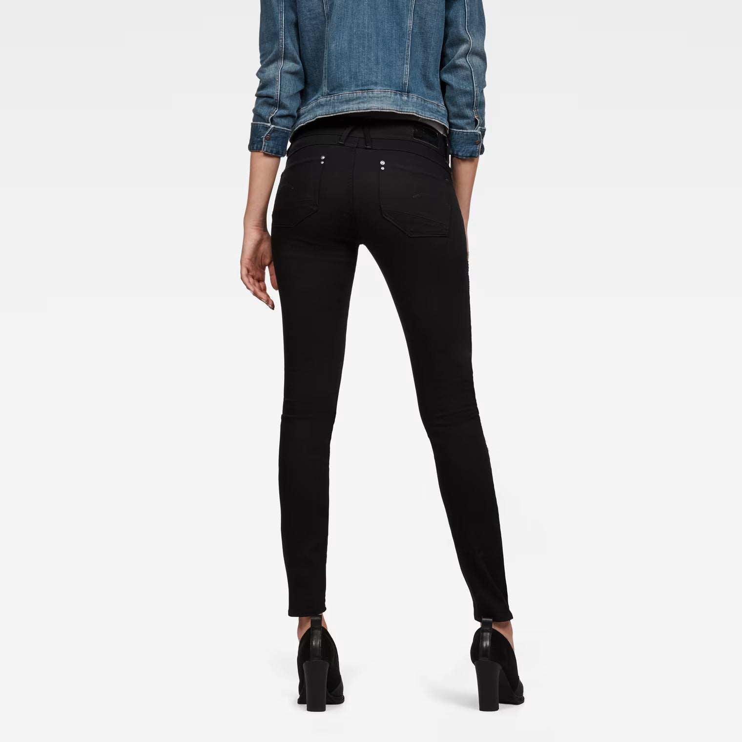 Back view of black skinny jeans featuring a mid-rise fit on a white background.