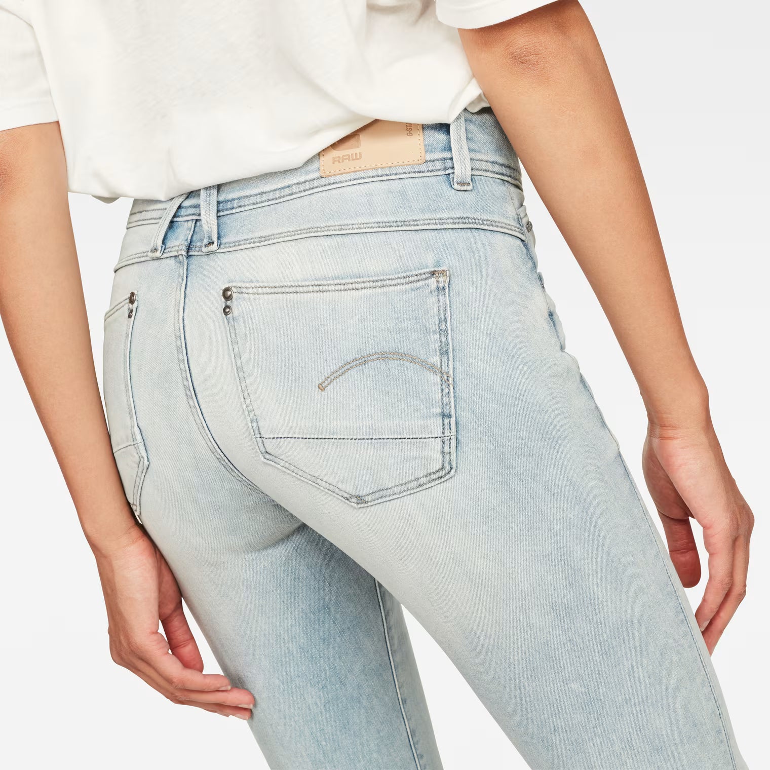 Detail shot of light blue skinny jeans highlighting the back pocket and mid waist on a white background.